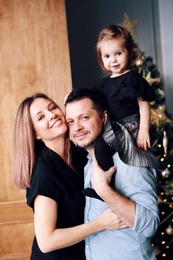 Gülümseyen, kucaklaşan güzel bir aile. Genç mutlu ebeveynler ve küçük kızları Noel ağacının yanında birlikte eğleniyorlar.