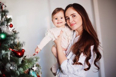 Mutlu güzel kadın Noel ağacının yanında kızıyla eğleniyor. Anne kollarında neşeli bir bebek tutuyor. 