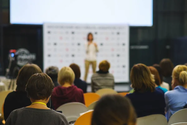 Back view of the participants of the seminar, training or lecture in a large audience with a large screen.