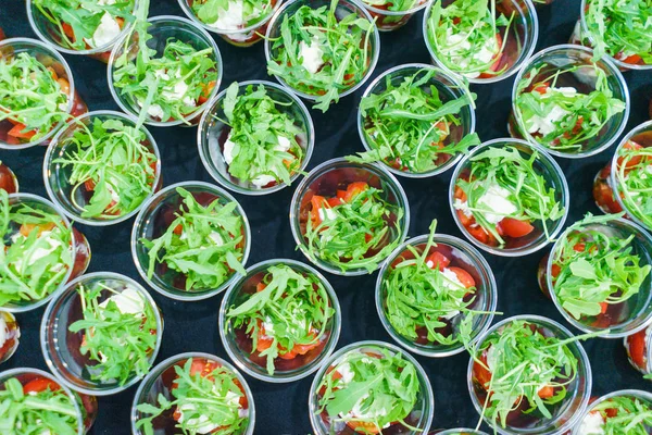 Mini appetizer salad in a glass, tomatoes with mozzarella, arugula and pesto.