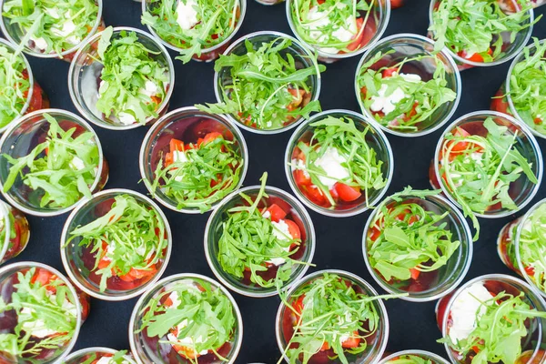Mini appetizer salad in a glass, tomatoes with mozzarella, arugula and pesto.