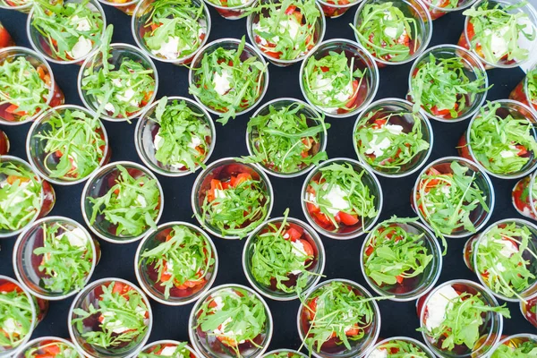 Mini appetizer salad in a glass, tomatoes with mozzarella, arugula and pesto.
