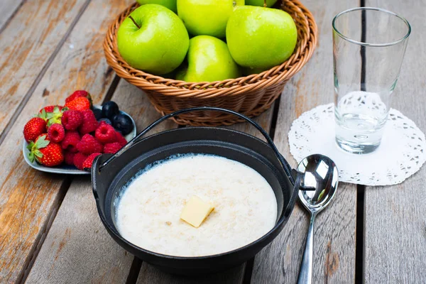 Traditional breakfast milk porridge with butter and berries on a wooden table.