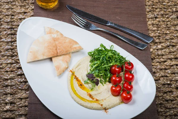 Traditional appetizer hummus with bread cakes, pita, on a plate with vegetables and sauce.