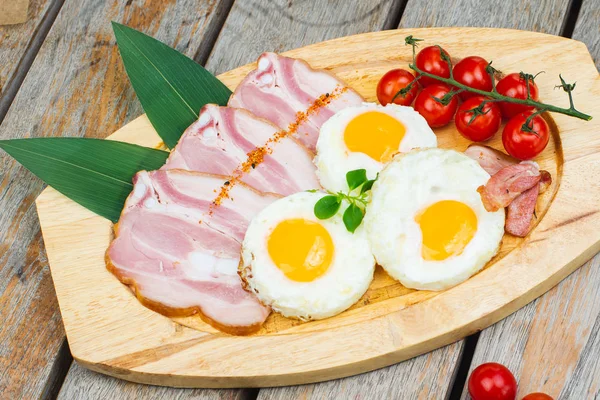 Tasty fried eggs with vegetables on a wooden plate.