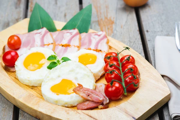 Tasty fried eggs with vegetables on a wooden plate.