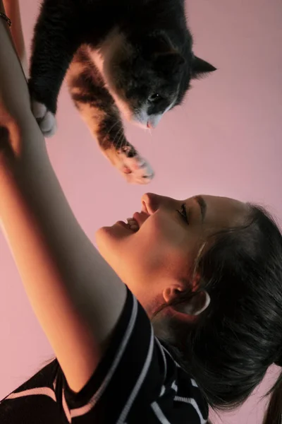 portrait of a young woman with a cat in her arms in red color lighting in the studio, girl raised up pet and playing with kitten