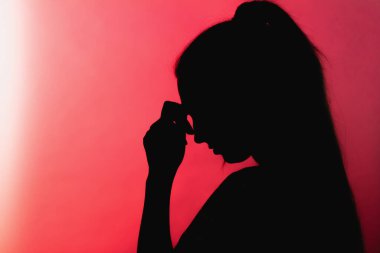 Alnında elleri olan üzgün bir kız silueti, kırmızı arka planda tanınmayan bir kadın yüzü, konsept hayat sorunları, endişe, yıkıcı duygular.