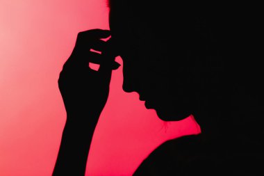 Alnında elleri olan üzgün bir kız silueti, kırmızı arka planda tanınmayan bir kadın yüzü, konsept hayat sorunları, endişe, yıkıcı duygular.