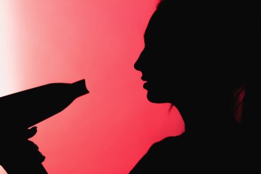 Güzel bir kadın profilinin silueti kırmızı arka planda saç kurutma makinesiyle saç stili yapıyor, güzellik ve tehlike kavramı.