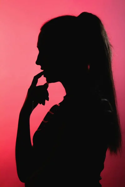 赤いライトアップの背景に思慮深い少女のシルエット 長い髪のポニーテールと認識できない女性のプロフィール コンセプト女性の美しさ — ストック写真