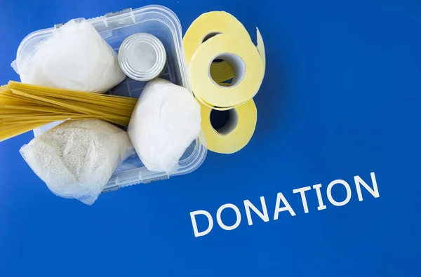 Food aid during quarantine. Container with products: sugar, rice, pasta, canned food. Food donation on a blue background. Help with products in the coronavirus.