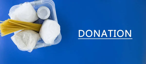 Food aid during quarantine. Container with products: sugar, rice, pasta, canned food. Food donation on a blue background. Help with products in the coronavirus. Banner.