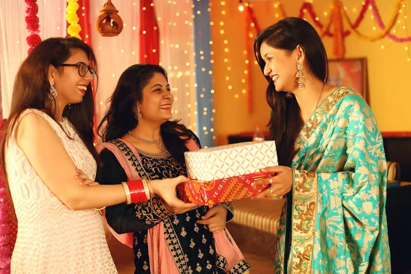 Young Indian women wearing traditional ethnic clothes giving gift to Friend. Isolated on decorative background.