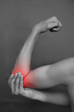 Gri arka planda dirseğinde ağrı hisseden bir adam.
