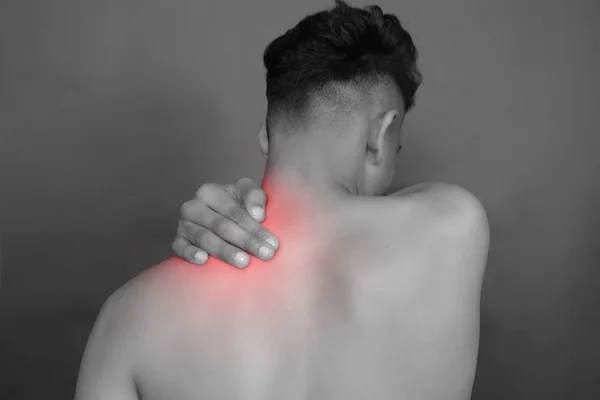 Black and white shot of man from back having red spot of pain and trauma in neck.