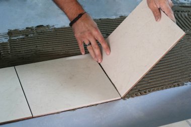 tiler bir spatula ile yapıştırıcı uygular. Seramik fayansları yere yapıştırır