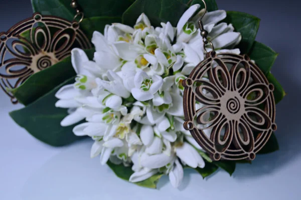 美しい木製のイヤリング 茶色のイヤリングは繊細な白い雪の花束に位置しています — ストック写真