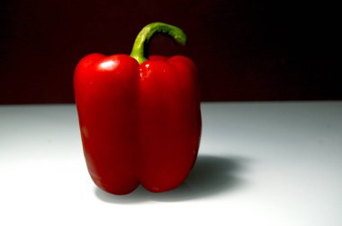 Kırmızı dolma biber, masada parlak sulu bir sebze yatıyor.