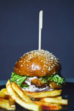 Lezzetli hamburger, susamlı taze çörek sebzelerin içinde pirzola ve sos, patates kızartmasının yanında.