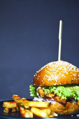 Lezzetli hamburger, susamlı taze çörek sebzelerin içinde pirzola ve sos, patates kızartmasının yanında.