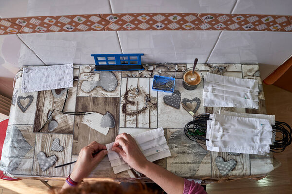 Woman's hands sewing cloth masks at home with a sewing machine to protect from the coronavirus.