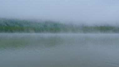 Sis ve bulutlar arasında dağlık siluet parçalarıyla kaplı bulutlu alp manzarası.