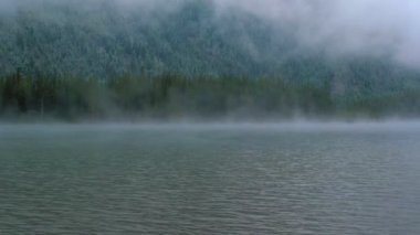 Sis ve bulutlar arasında dağlık siluet parçalarıyla kaplı bulutlu alp manzarası.