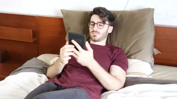 Młody człowiek na łóżku czytając z ebook reader — Wideo stockowe