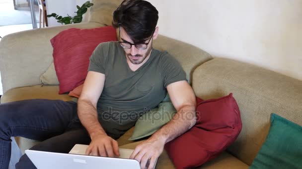 Mladý muž dělá domácí práce na notebooku na pohovce — Stock video