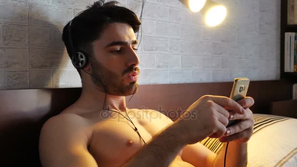 Young man in bed listening to music with headphones — Stock Video