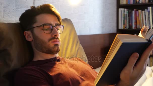 Joven acostado en la cama y leyendo un libro — Vídeos de Stock