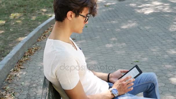 Jovem no parque da cidade usando leitor de ebook — Vídeo de Stock