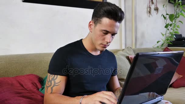 Mladý muž dělá domácí práce na notebooku na pohovce — Stock video
