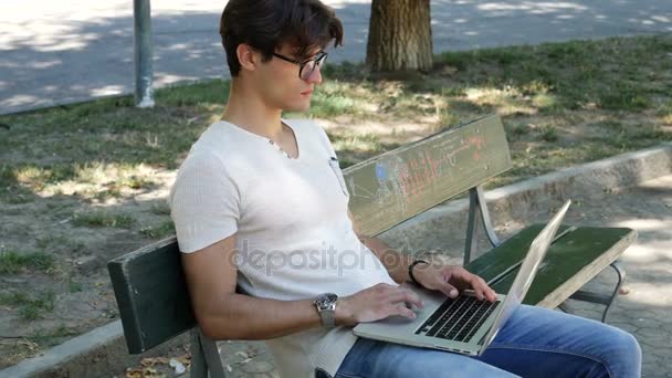 Jovem bonito trabalhando no computador no parque — Vídeo de Stock