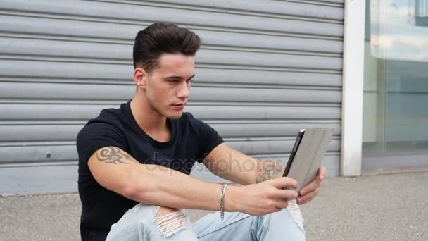 Молодой человек, использующий планшетный компьютер на открытом воздухе в городе — стоковое видео