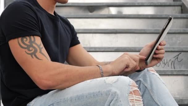 Hombre de moda guapo mirando hacia abajo en una tableta, al aire libre — Vídeos de Stock