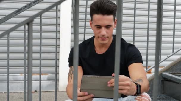 Bonito homem da moda olhando para baixo em um computador tablet, ao ar livre — Vídeo de Stock