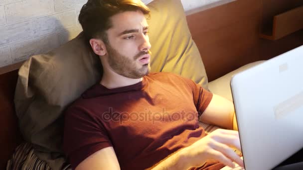 Hombre joven haciendo la tarea en el ordenador portátil en el dormitorio — Vídeos de Stock