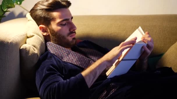 Jovem deitado na cama e lendo um livro — Vídeo de Stock