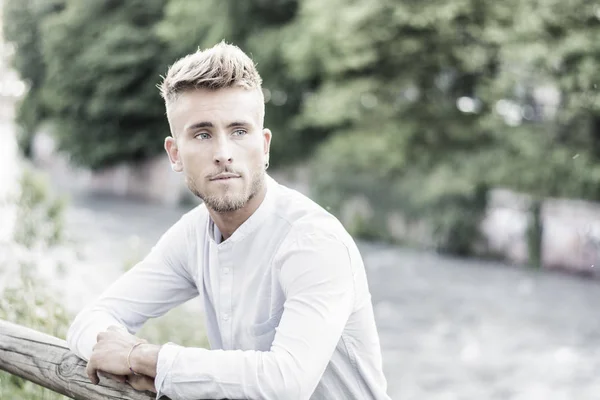 Blondish, blue eyed young man by river smiling — Stock Photo, Image