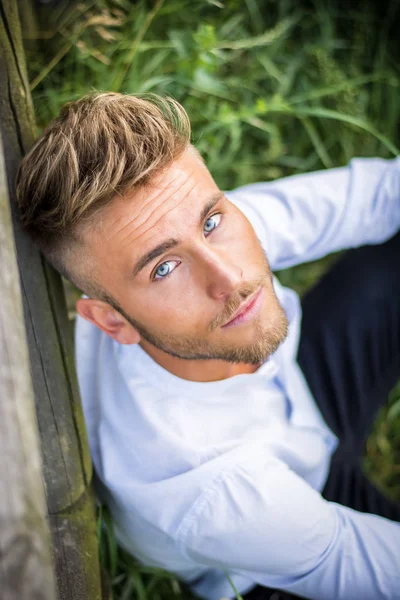 Blondish, blue eyed young man on wood fence — Stock Photo, Image