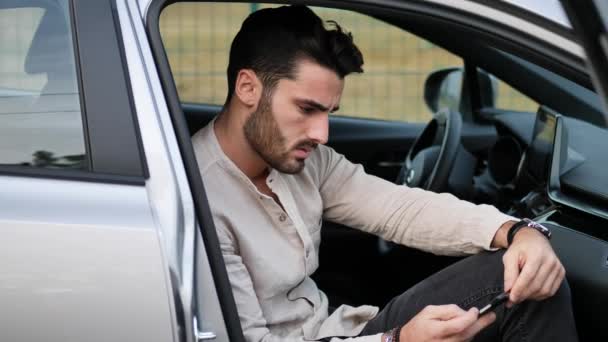 Hombre joven usando el teléfono móvil sentado en el coche — Vídeo de stock