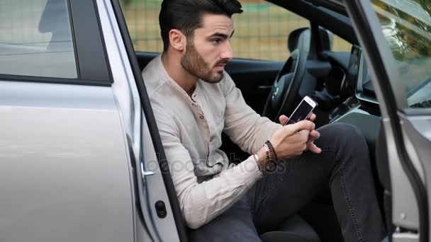Молодой человек с помощью мобильного телефона сидит в машине — стоковое видео