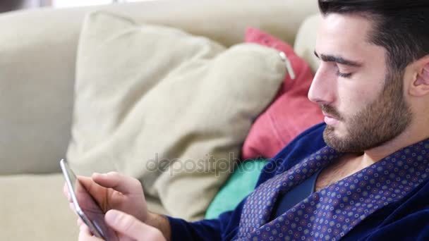 Молодой человек на диване чтение с планшетного компьютера — стоковое видео