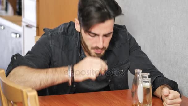 Joven sentado bebiendo solo en una mesa con dos botellas de licor — Vídeo de stock