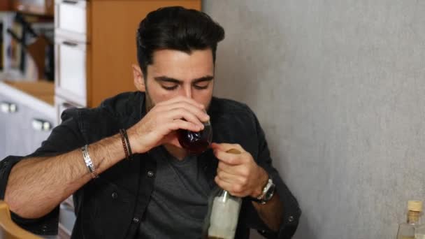 Joven sentado bebiendo solo en una mesa con dos botellas de licor — Vídeos de Stock