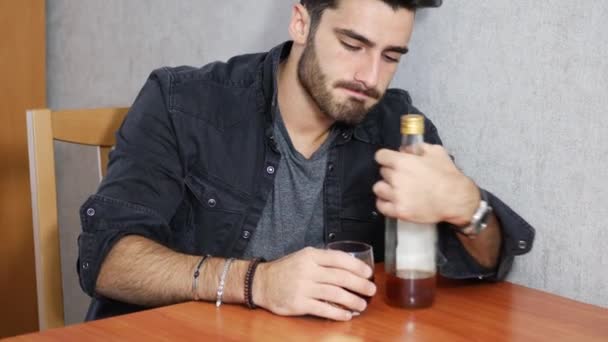Ung man sitter dricka ensam vid ett bord med två flaskor med sprit — Stockvideo