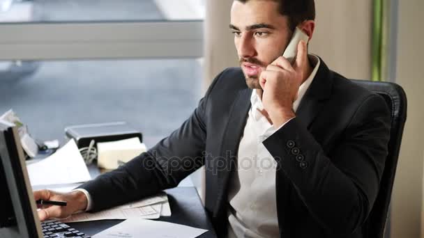 Feliz joven empresario en el teléfono, sentado en el escritorio — Vídeos de Stock