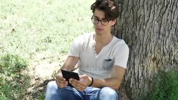 Jonge man in stadspark met behulp van ebook reader — Stockvideo